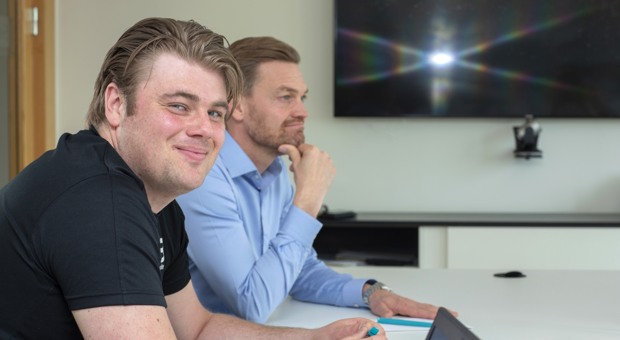 Två kollegor samtalar varav den ena tittar in i kameran.