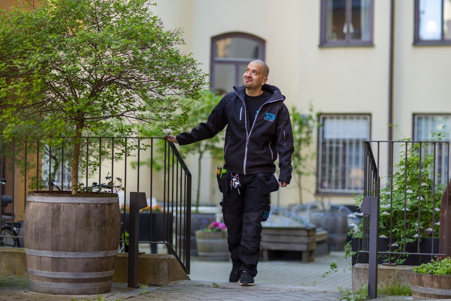 Arbetsklädd man går uppför liten trappa på innergård. Han håller sig i ett metallräcke med ena handen. Blicken är riktad snett uppåt.