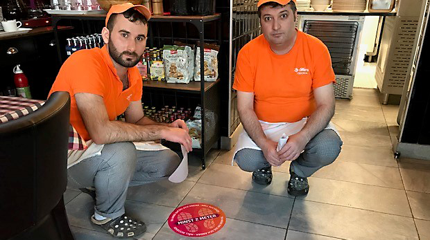 Två pizzabagare placerar dekal om att hålla avstånd på golvet