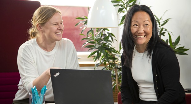 Två kollegor skrattar framför en dator