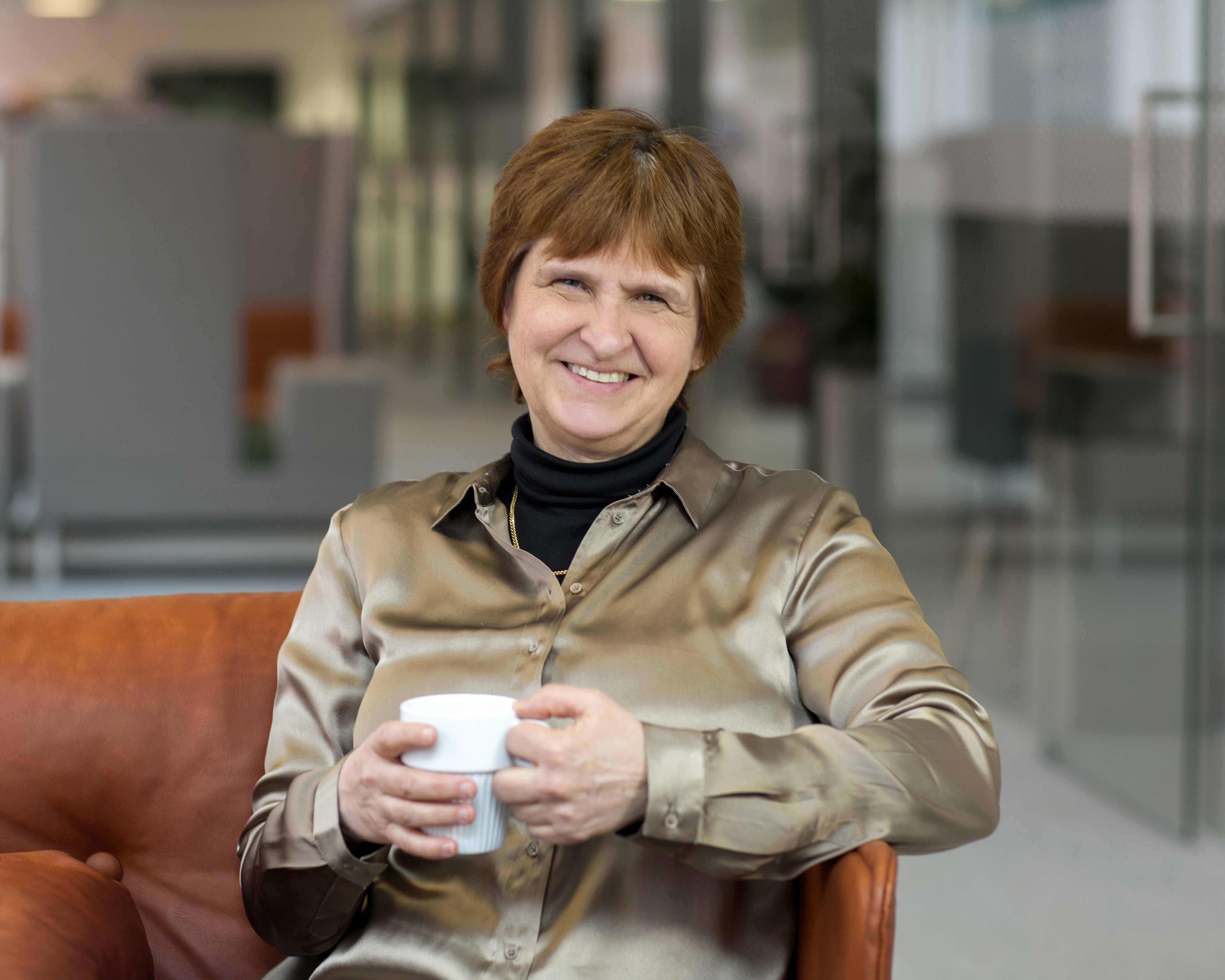 En kvinna sitter i en fåtölj med en kopp kaffe i handen.