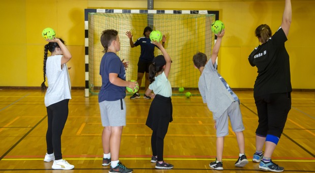 Barn kastar bollar mot målvakten i handboll.
