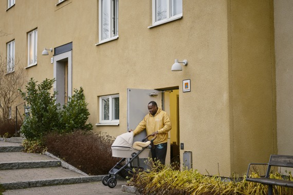 En man med barnvagn kommer ut ur en ytterdörr på en fastighet. Bredvid dörren sitter en skyddsrumsskylt.