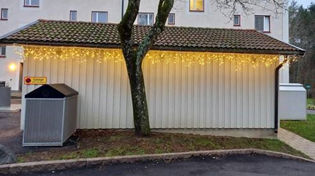 Lysande juldekoration längs med takets underkant på vit träbyggnad utanför fastighet.