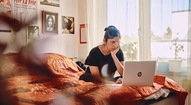 Kvinna sitter på säng med en laptop.