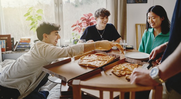 Kompisar äter pizza ihop vid köksbordet.